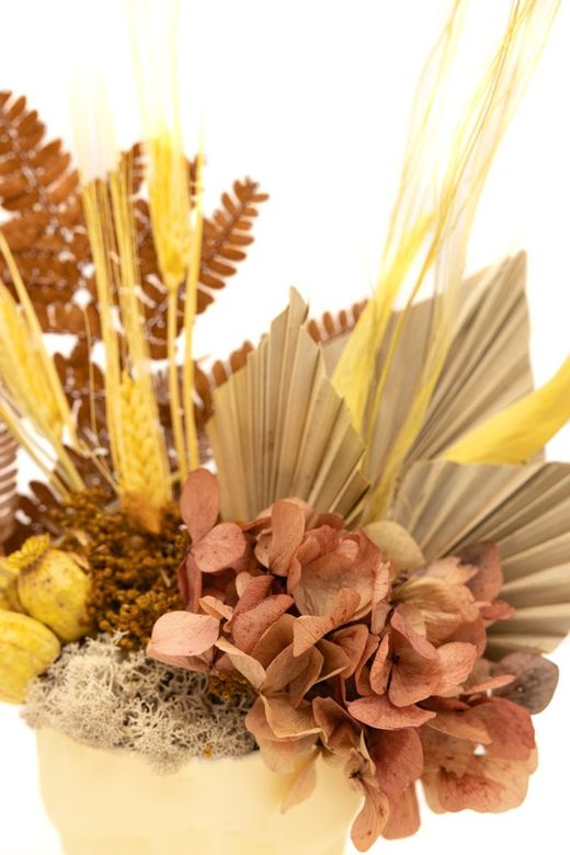 Centro de mesa con base en tono mostazo con flores preservadas amarillas, crema y mostaza